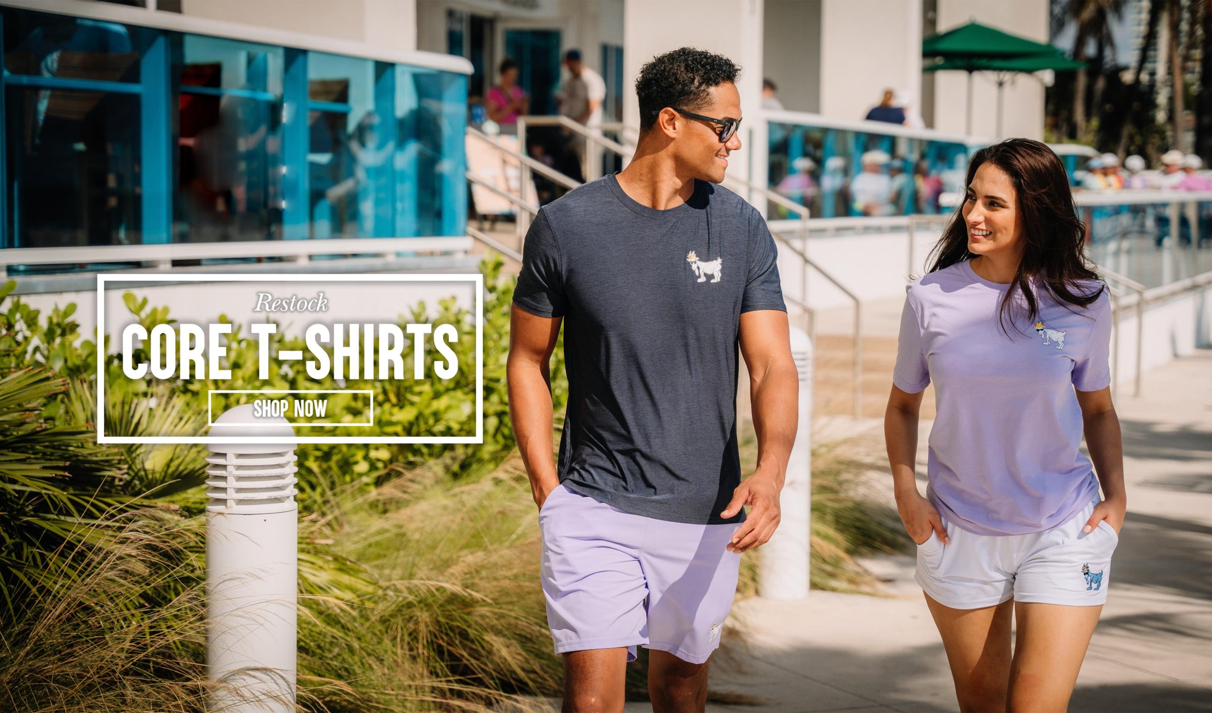 Man and woman walking through beach town on a sunny day with text that reads "Restock Core T-Shirts Shop Now"