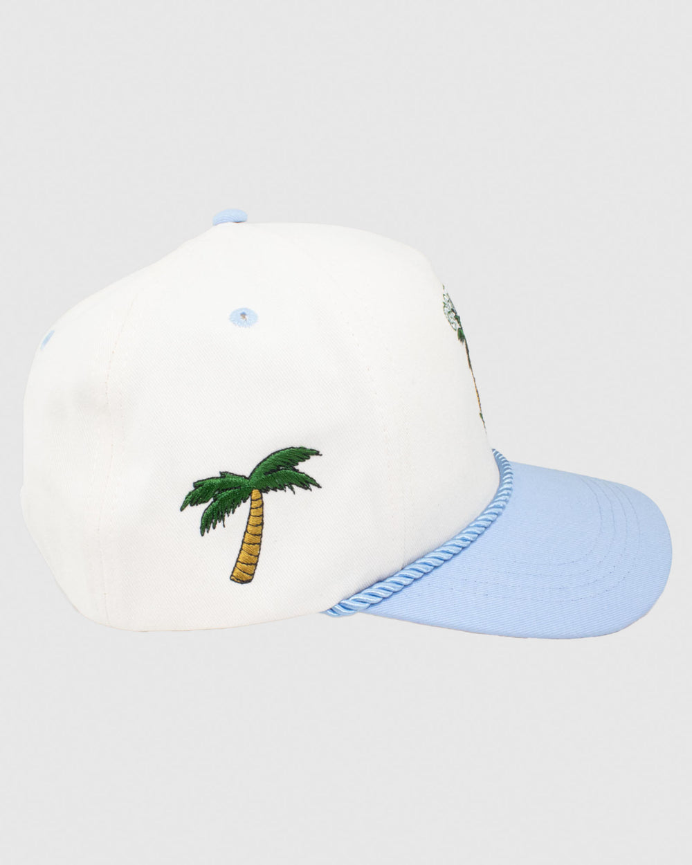 Side view of cream hat with blue rope and brim. Features a palm tree sunset design