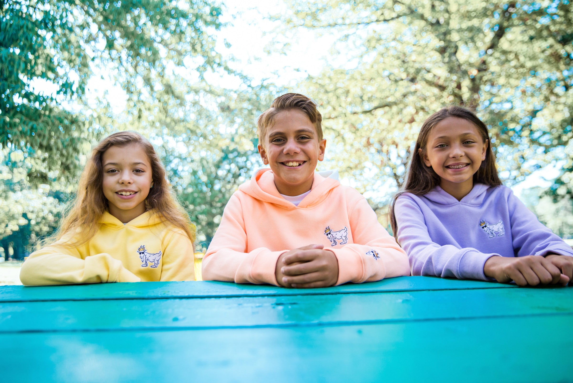 children sitting at a park bench wearing sweatshirts