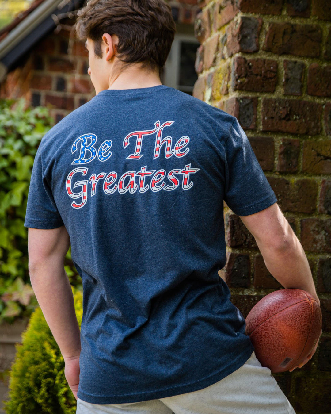 Model wearing navy Freedom Be the Greatest T-Shirt with football#color_navy
