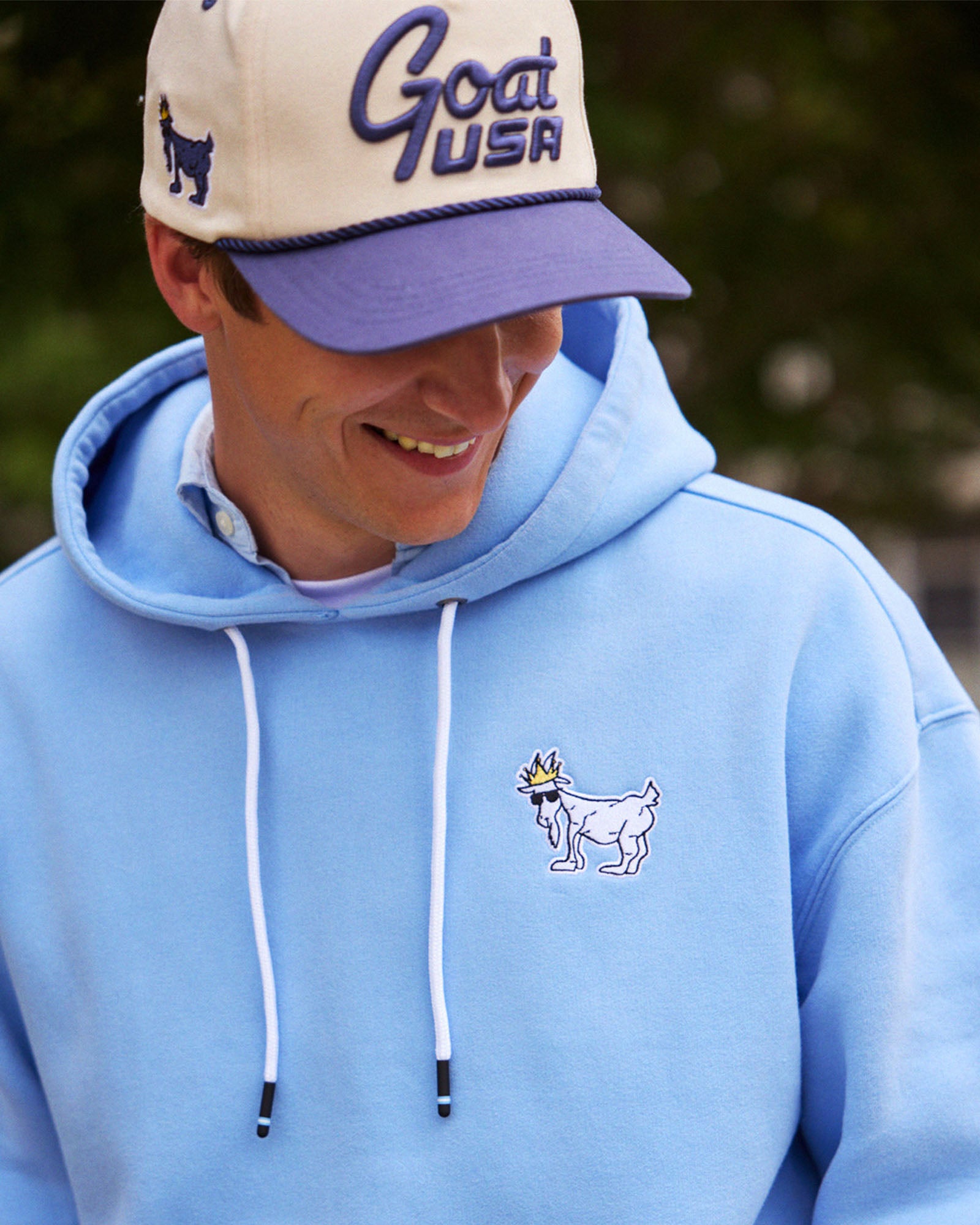 Person wearing a light blue hoodie with a goat graphic and a matching cap outdoors.