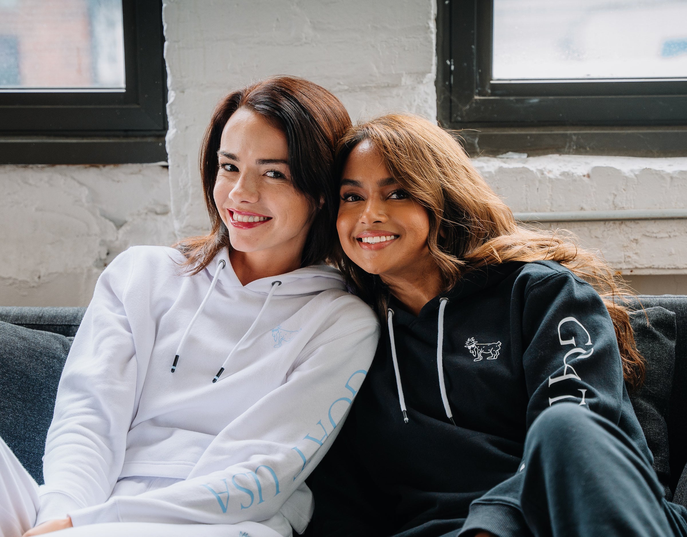 Two women sitting on couch wearing matching sweats sets