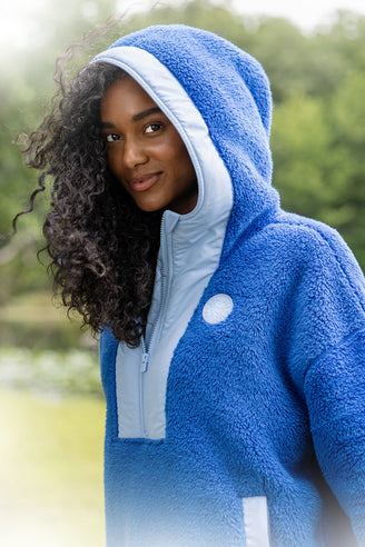 Person wearing a blue fleece hoodie with a blurred natural background