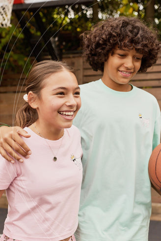 Two children standing together, one holding a basketball, with a casual outdoor setting.