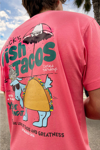 Person wearing a salmon-colored t-shirt with a graphic design on the back, featuring text and an illustration of a fish taco.