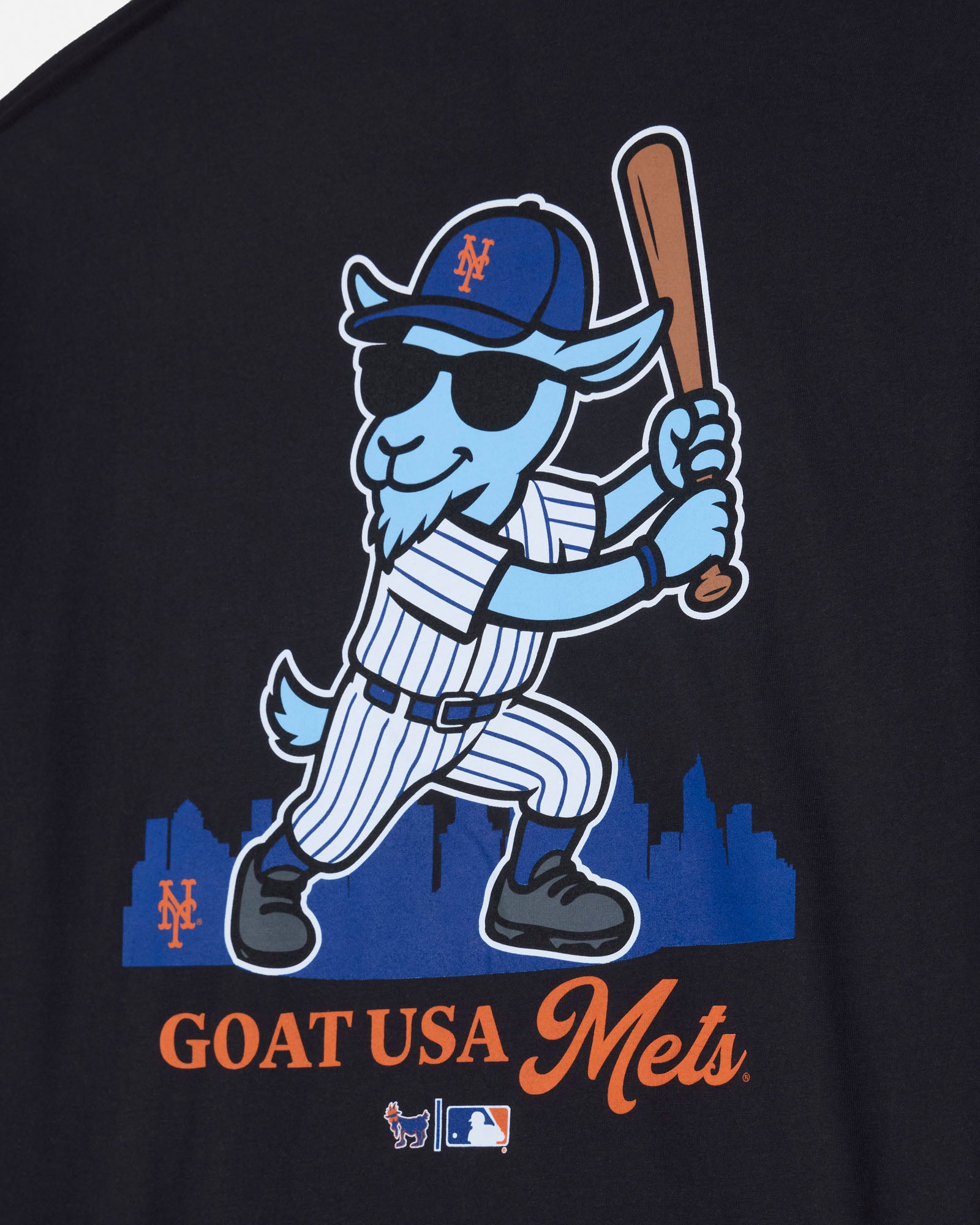 Close-up of a black graphic T-shirt featuring a cartoon goat baseball player in a blue and white pinstripe uniform, holding a bat, with 'GOAT USA Mets' text below.