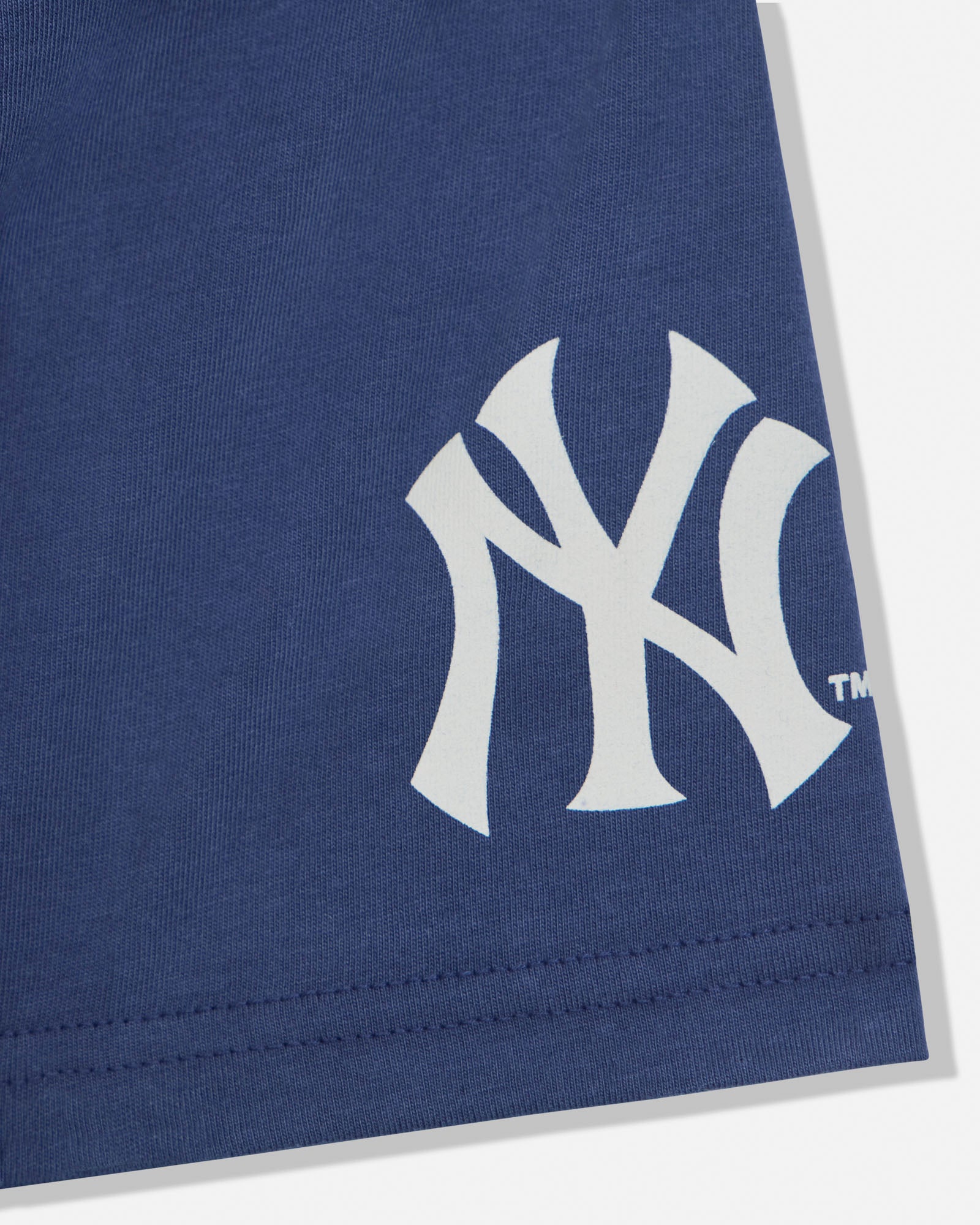 Close-up of a navy blue fabric product featuring a large white New York Yankees interlocking NY logo and a small TM mark, with visible stitching along the bottom edge.