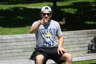 Man sitting on a park bench pointing towards the camera