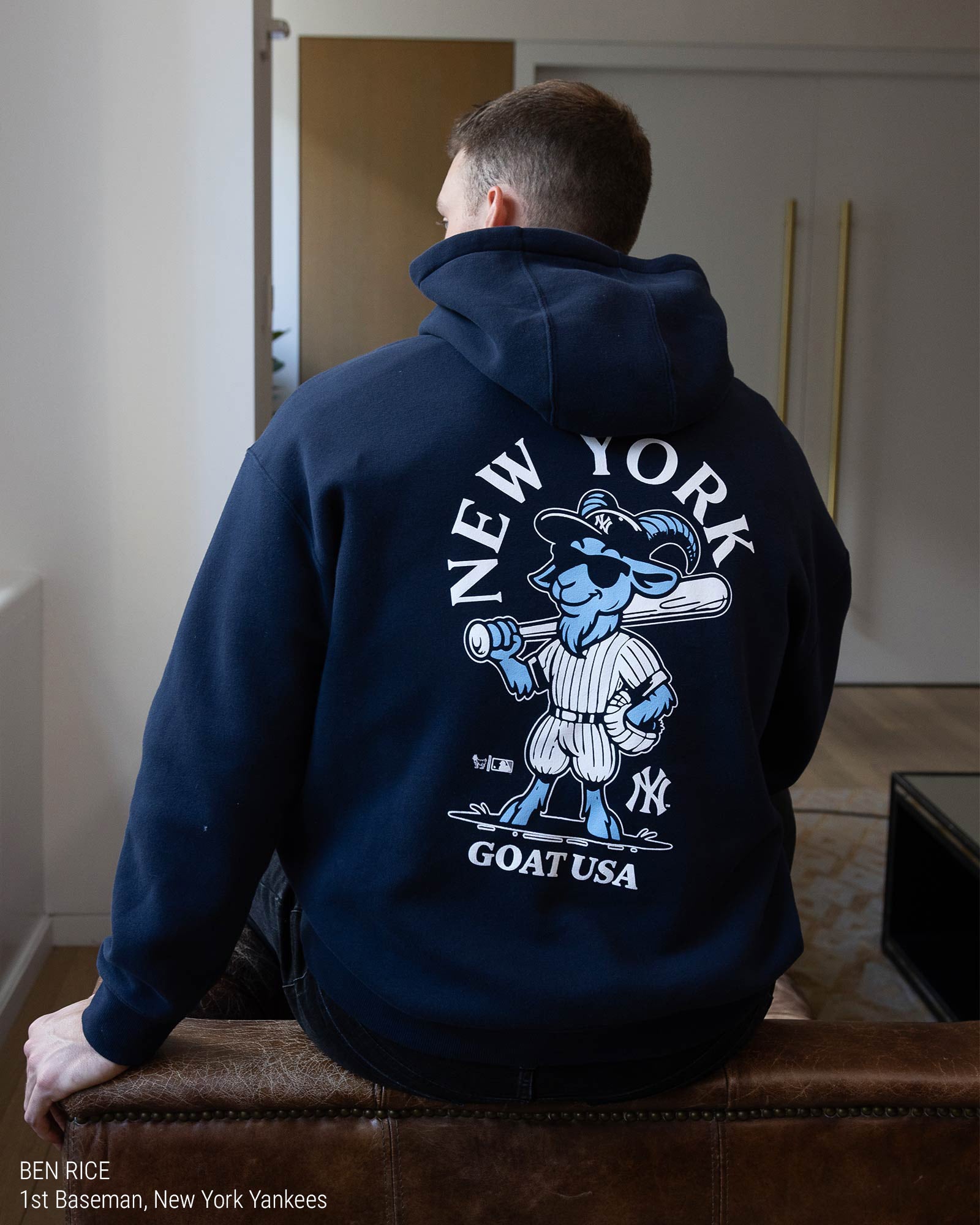 Ben Rice in a navy blue hoodie shown from the back, featuring a white graphic print of the New York Yankees logo with the word 'YANKEES' and a goat illustration on a light gray background.#color_navy