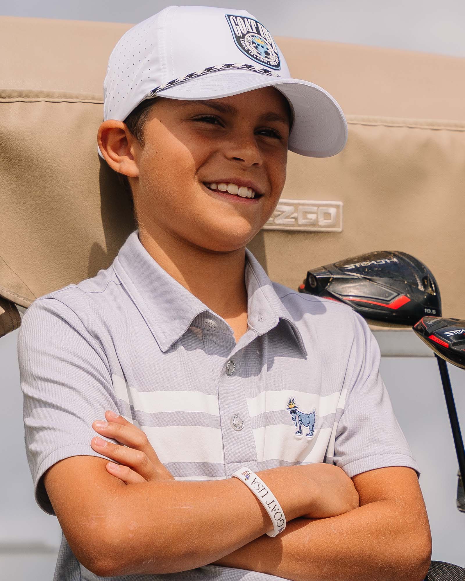 Child wearing a cap and polo shirt with golf clubs in the background