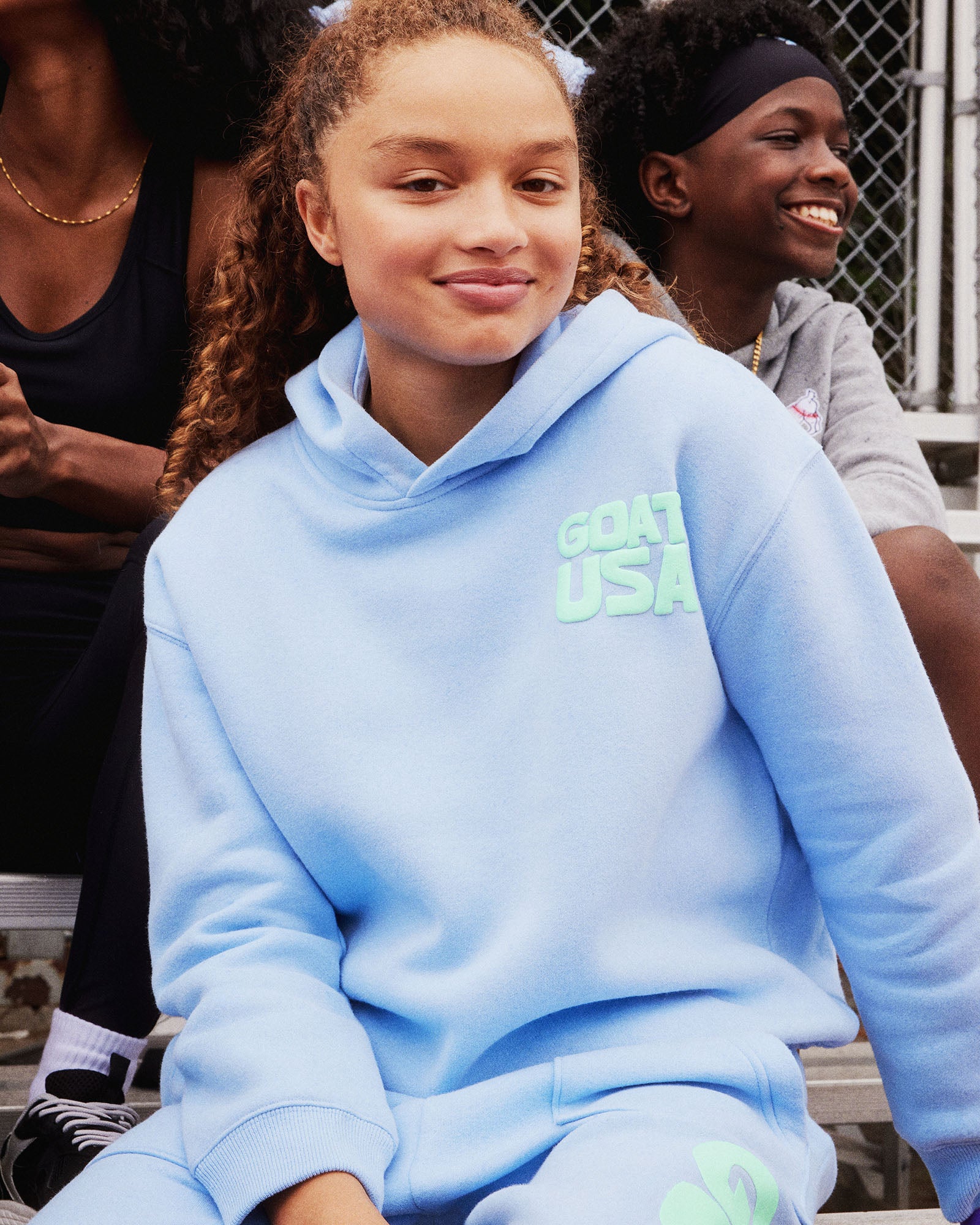 Person wearing a light blue hoodie with 'GOAT USA' text, sitting outdoors.