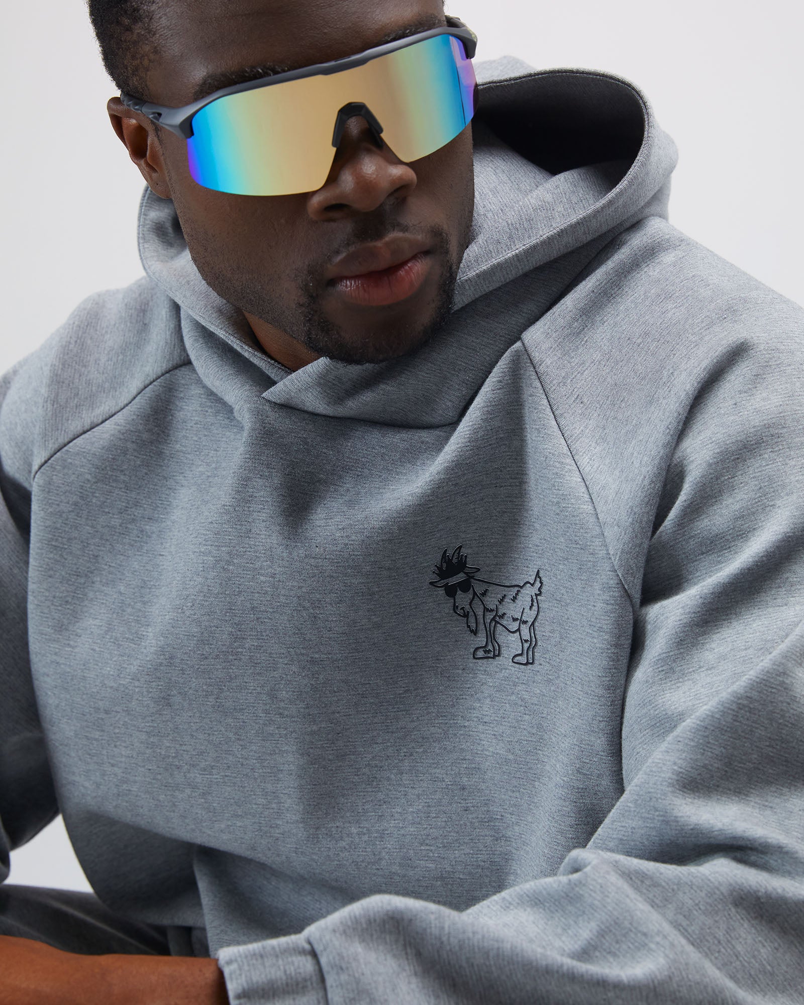 Person wearing a gray hoodie with a small logo, sitting against a plain background