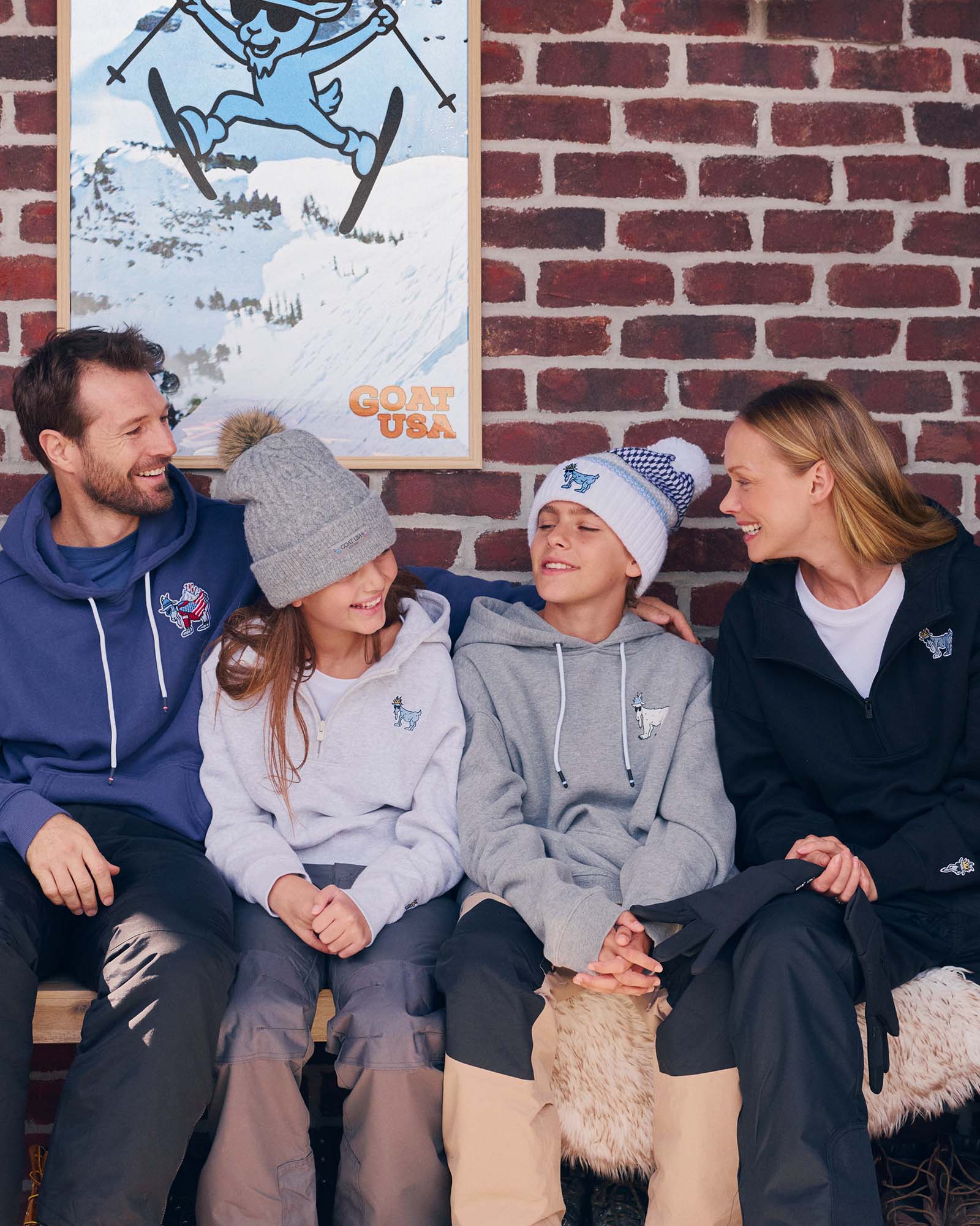 Family sitting together wearing matching hoodies in front of a brick wall with a skiing poster.