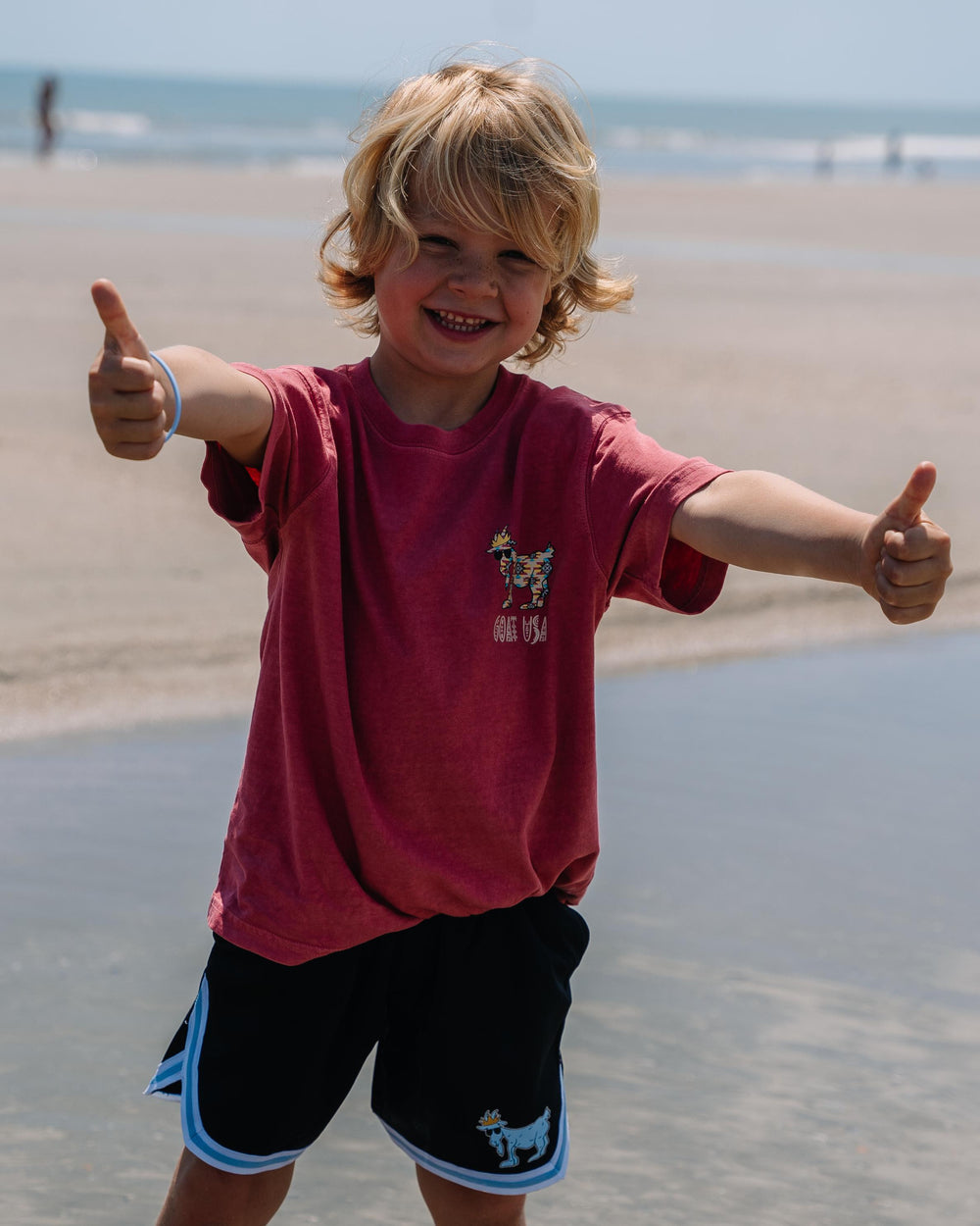 Kid smiling with two thumbs up on a beach