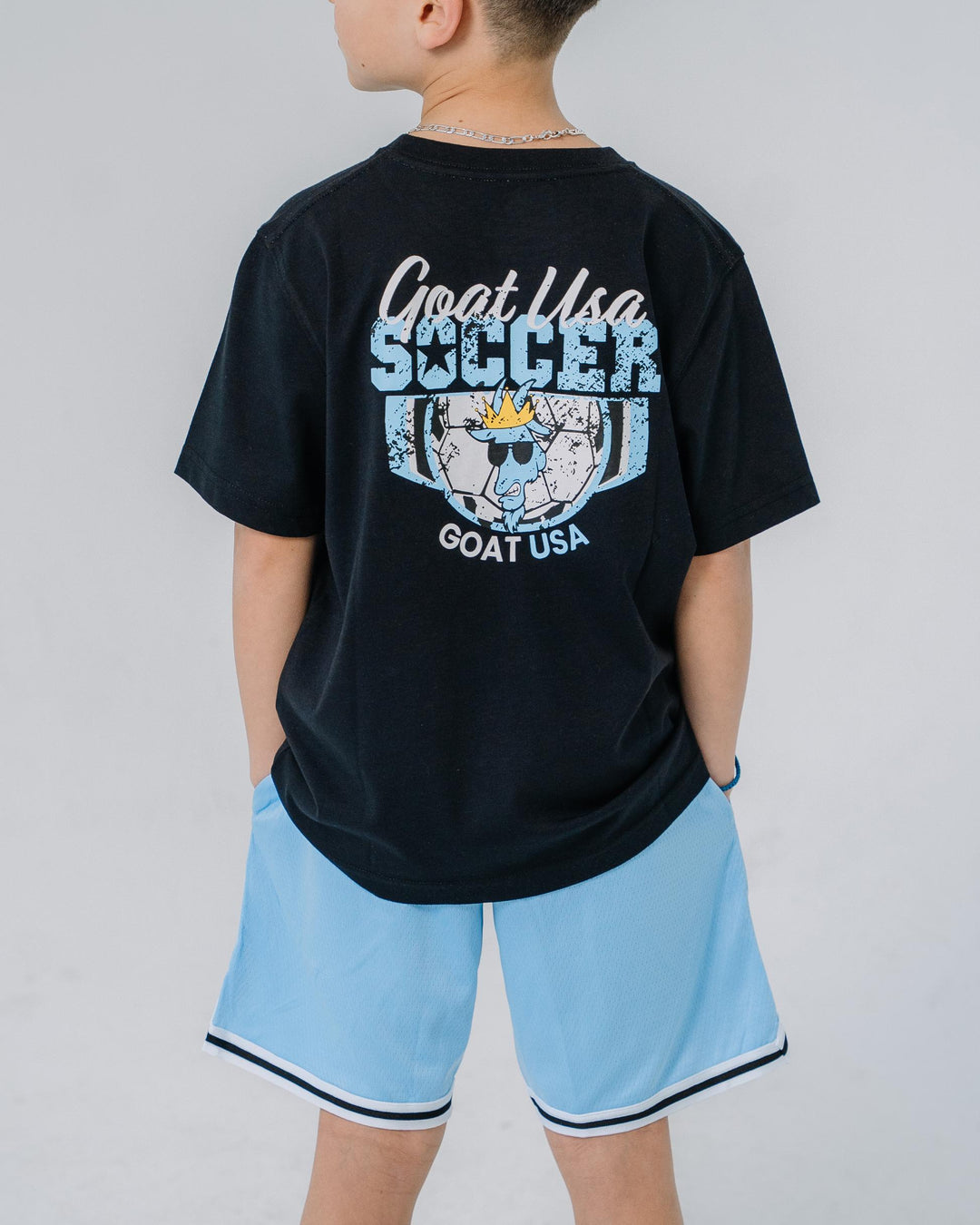 Kid wearing black t-shirt with soccer design that reads "GOAT USA SOCCER"