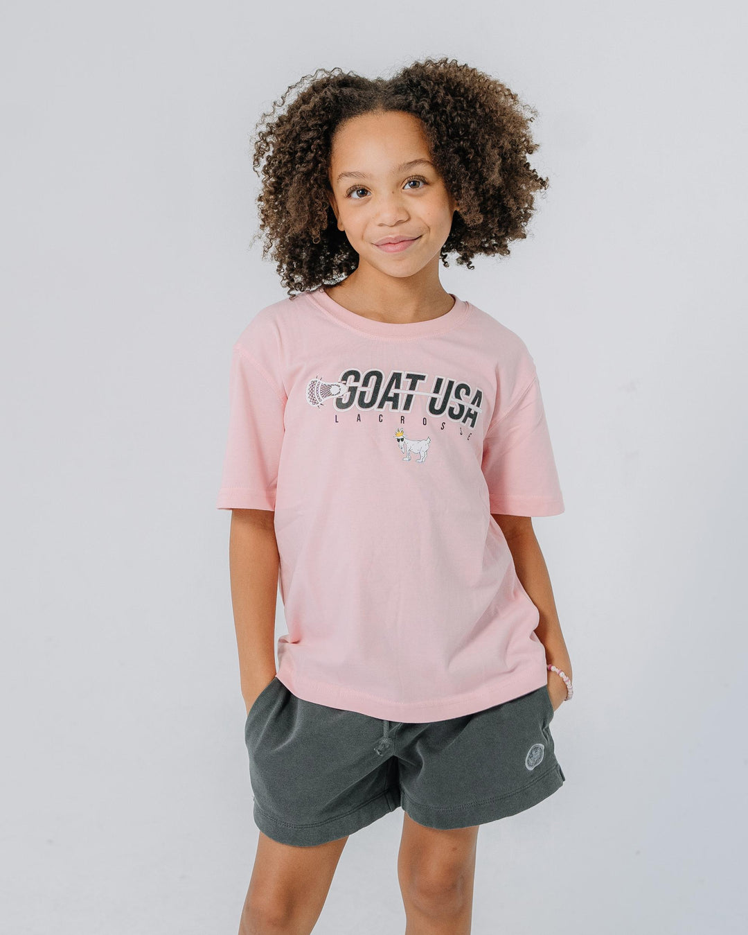 Girl wearing pink shirt with lacrosse stick that goes through the wording "GOAT USA"#color_pink