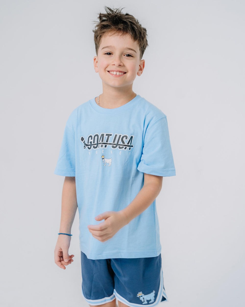 Kid wearing carolina blue shirt with hockey stick that goes through the wording "GOAT USA"