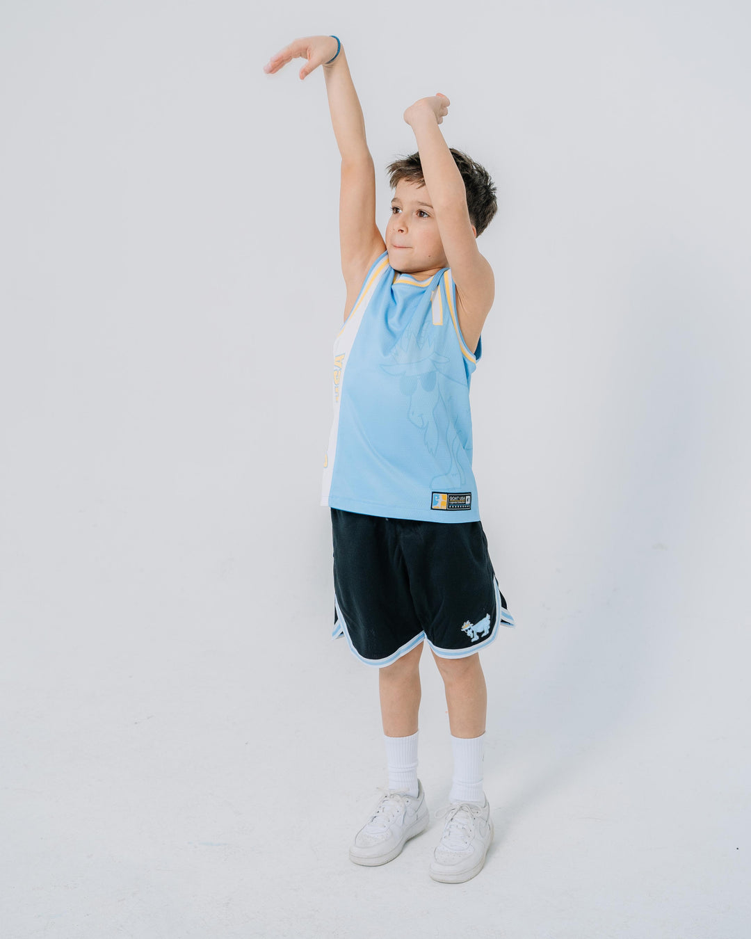Kid holding a basketball shooting pose  wearing a carolina blue, white and gold jersey with goat design that wraps around