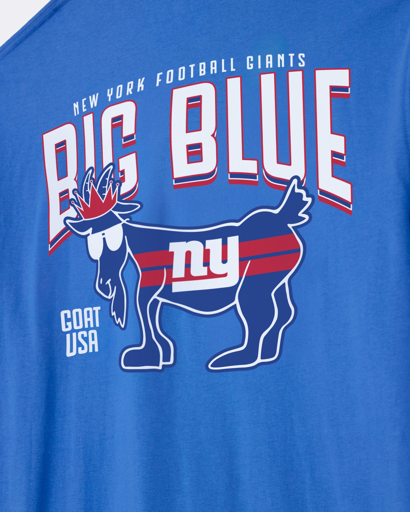 A close-up of a blue t-shirt featuring a New York Football Giants graphic. The design includes the words 'NEW YORK FOOTBALL GIANTS', 'BIG BLUE' in large white letters with red and blue outlines, a blue goat mascot with 'ny' on its back, and 'GOAT USA' printed on the lower left.