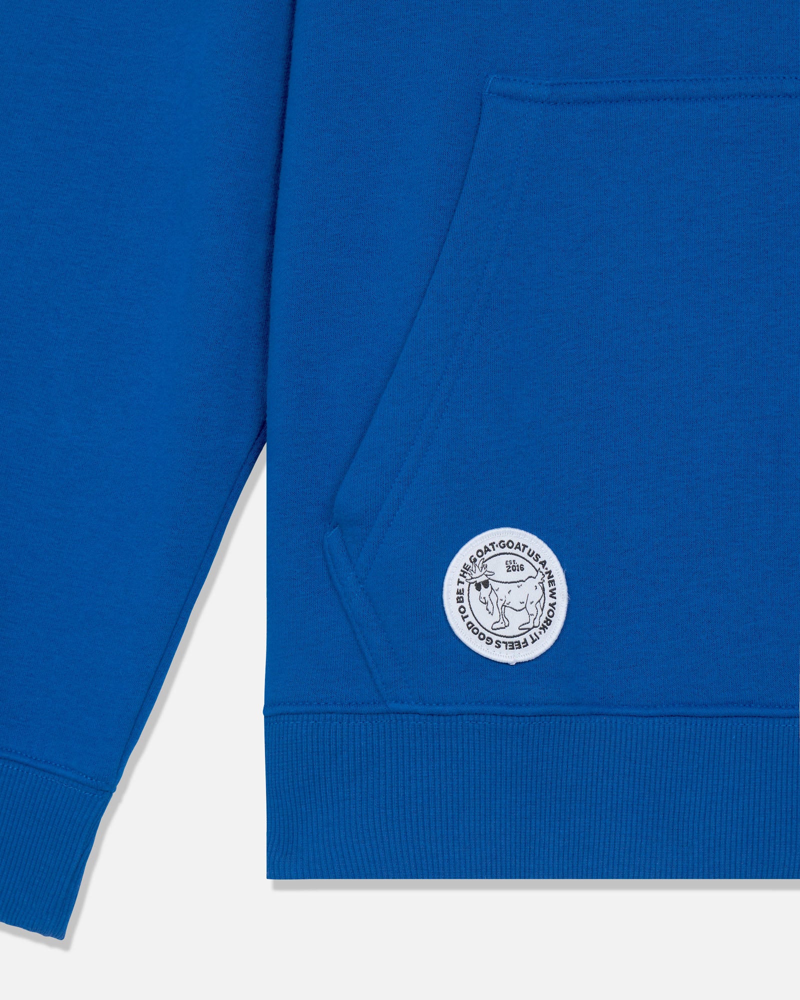 Close-up of a royal blue sweatshirt showing the left chest pocket and a circular white embroidered logo patch on the lower front.