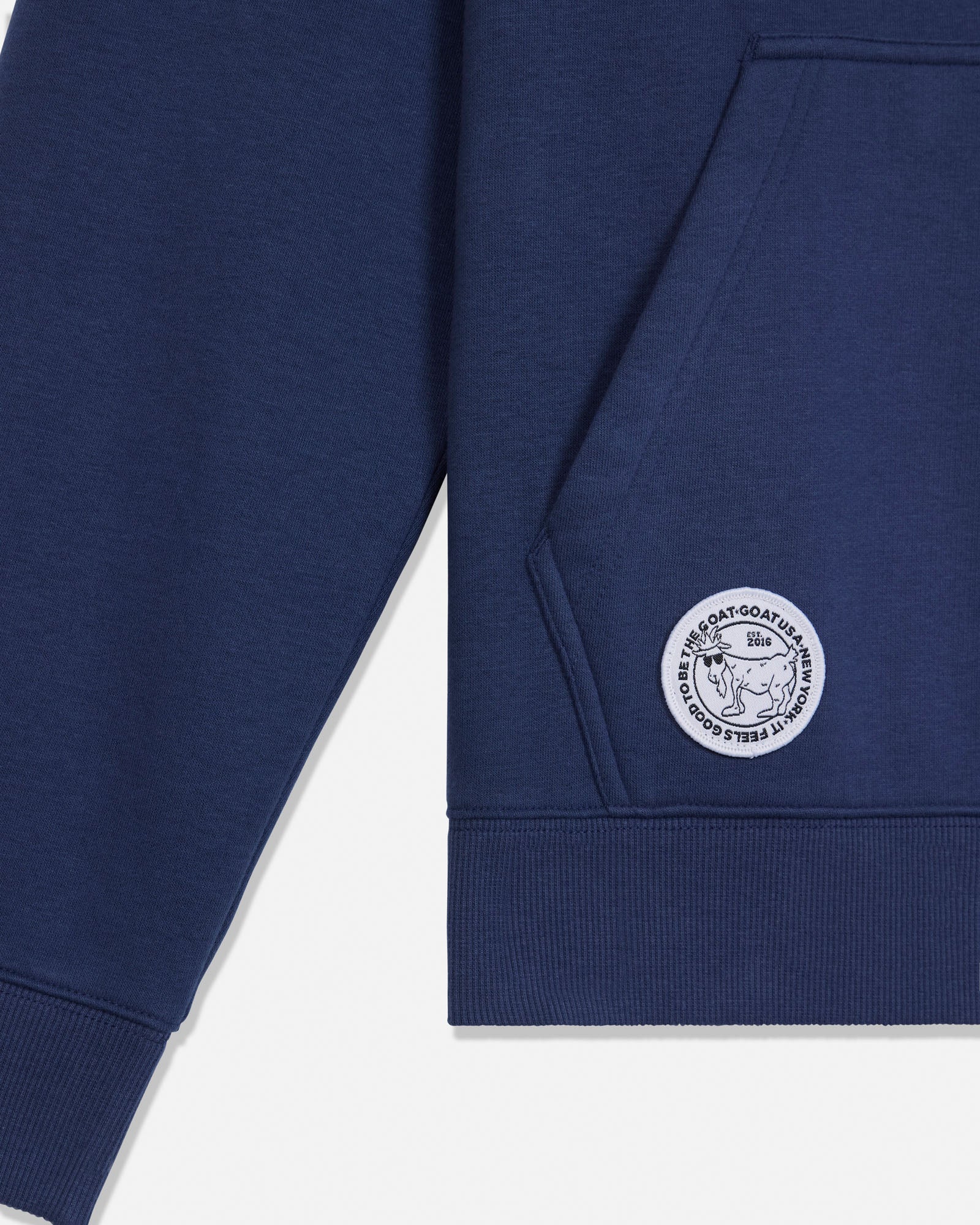 Close-up of a navy blue sweatshirt sleeve and pocket corner with a circular white embroidered logo patch on the pocket.
