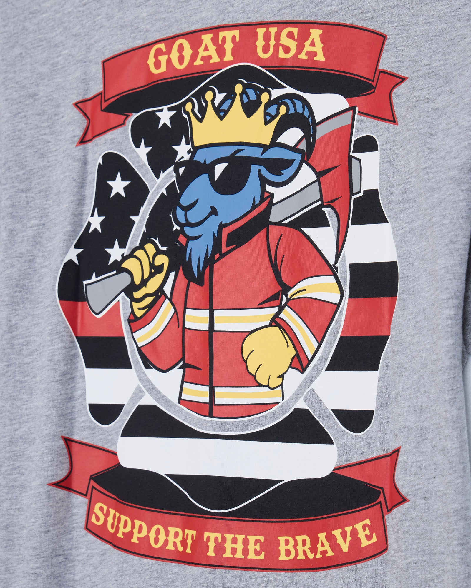 Close-up of a heather gray sweatshirt featuring a large graphic print of a blue goat wearing a gold crown and sunglasses, dressed in a red firefighter jacket, with a black-and-white striped shield and red banners reading 'GOAT USA' and 'SUPPORT THE BRAVE'.