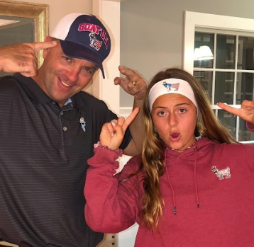 Father and daughter pointing to their GOAT USA headwear in an indoor setting