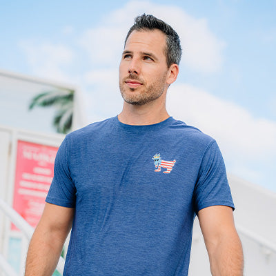 Male wearing GOAT USA navy athletic t-shirt outdoors on a sunny day.