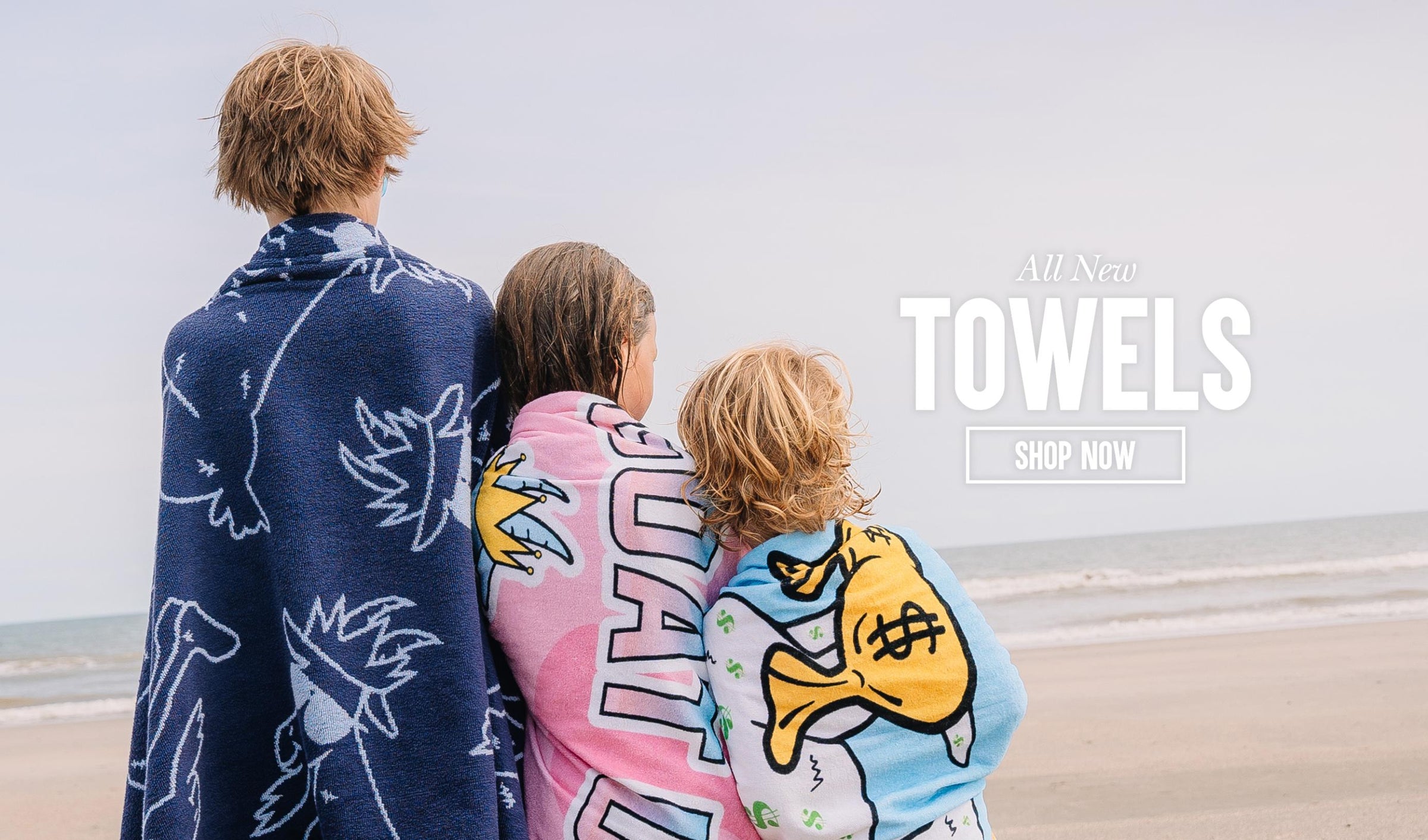 Three kids wrapped in towels on the beach looking at the ocean