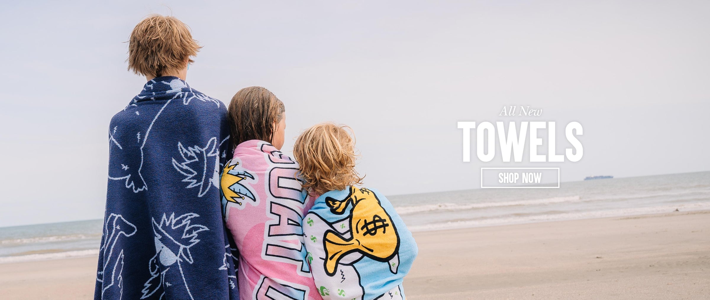 Three kids wrapped in towels on the beach looking at the ocean
