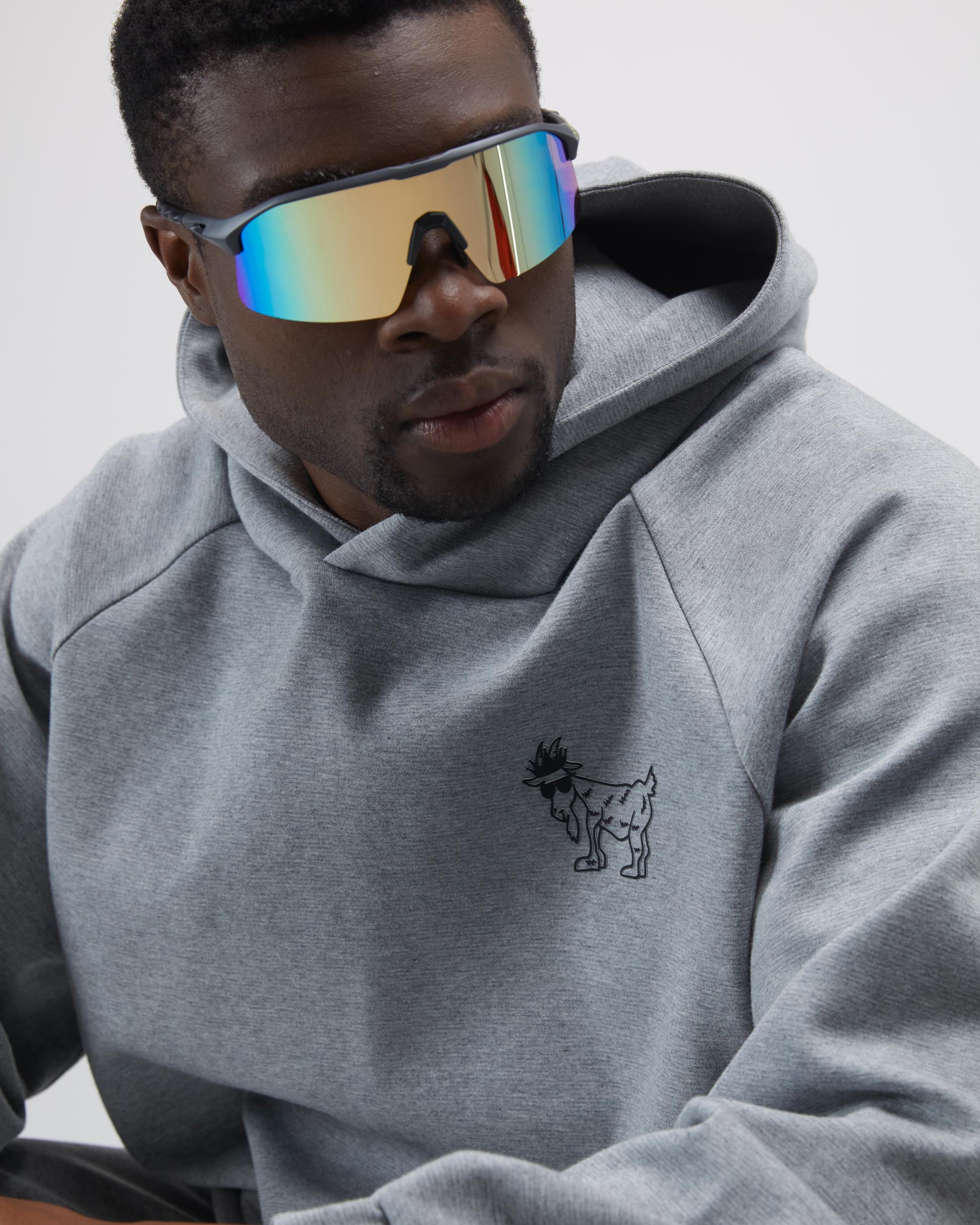 Person wearing a gray hoodie with a small logo, sitting against a plain background#color_gray