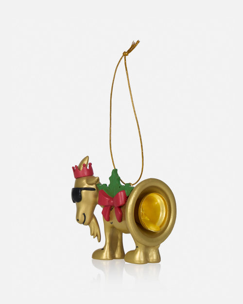 A gold-toned Christmas ornament shaped like a goat wearing a pink crown, black sunglasses, a green wreath, and a pink bow, with a gold hanging string.