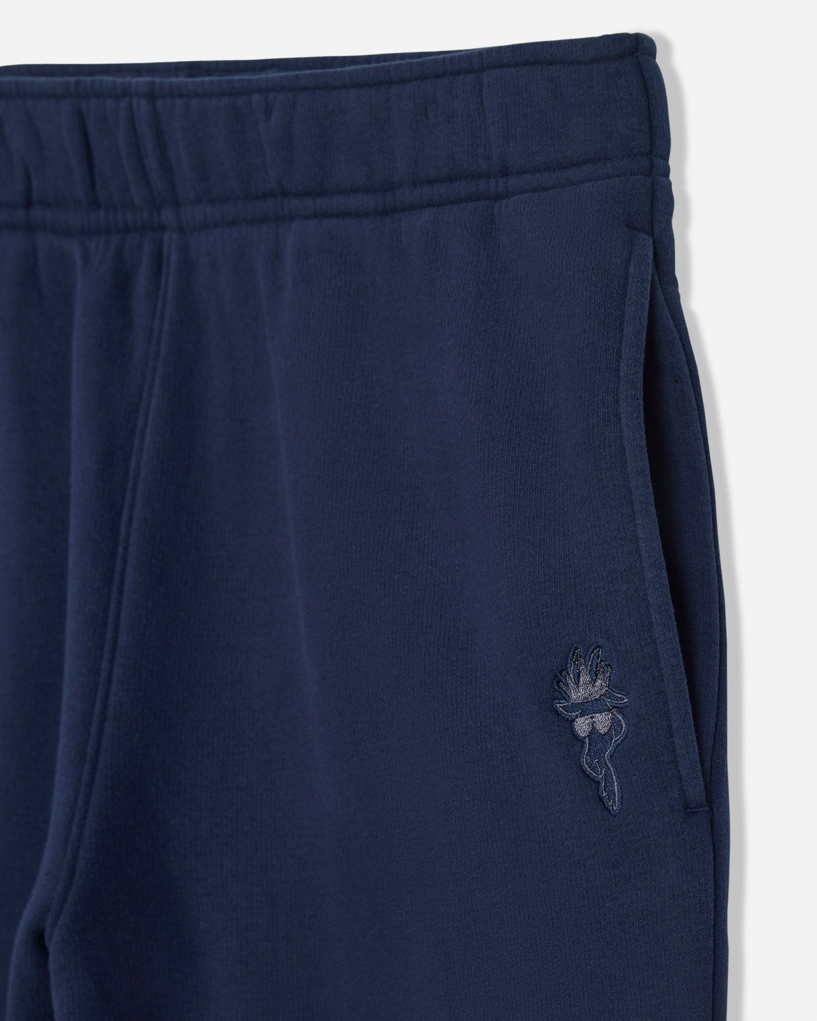 Close-up of navy blue sweatpants showing the elastic waistband, side pocket, and a small tonal embroidered logo on the thigh.#color_navy-blazer