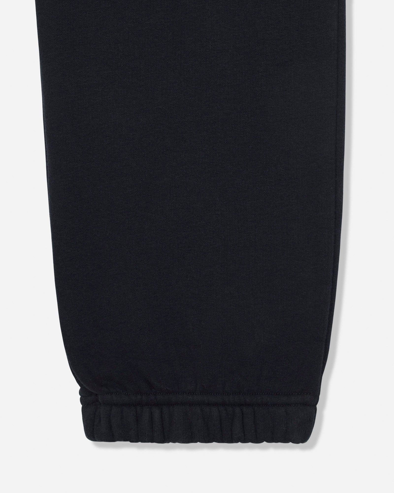 Close-up of a black fabric garment leg with an elasticized cuff, shown against a light gray background.#color_black