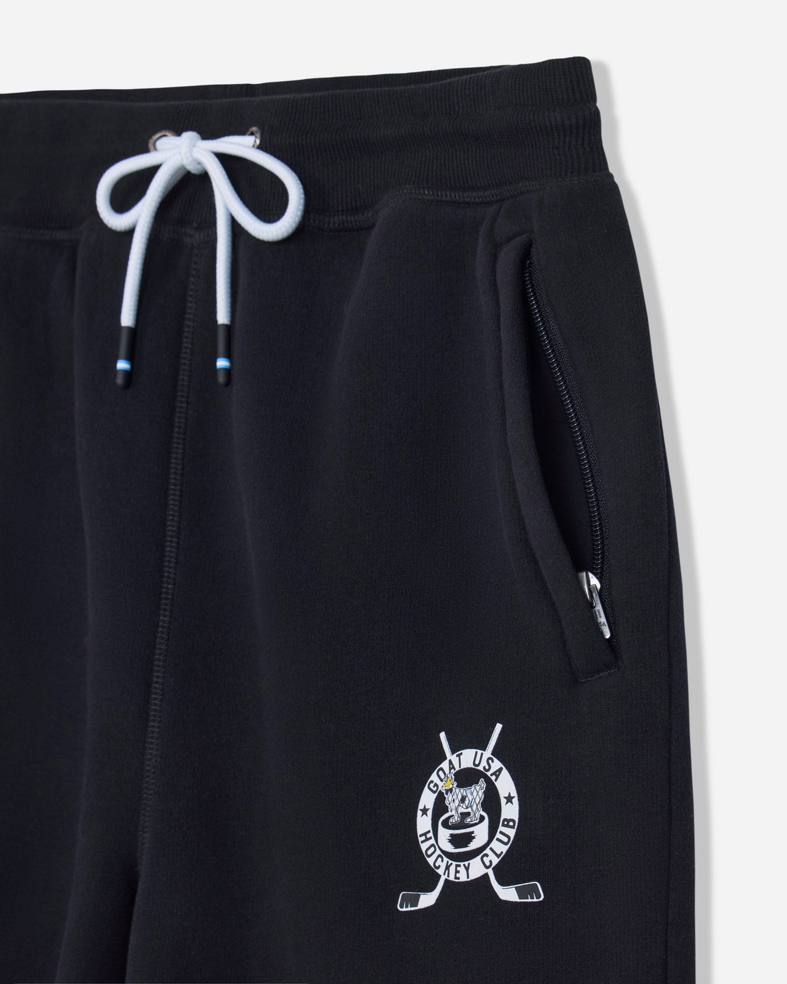 Close-up of black sweatpants with a white drawstring, side zip pocket, and a white hockey-themed crest logo near the lower left leg.