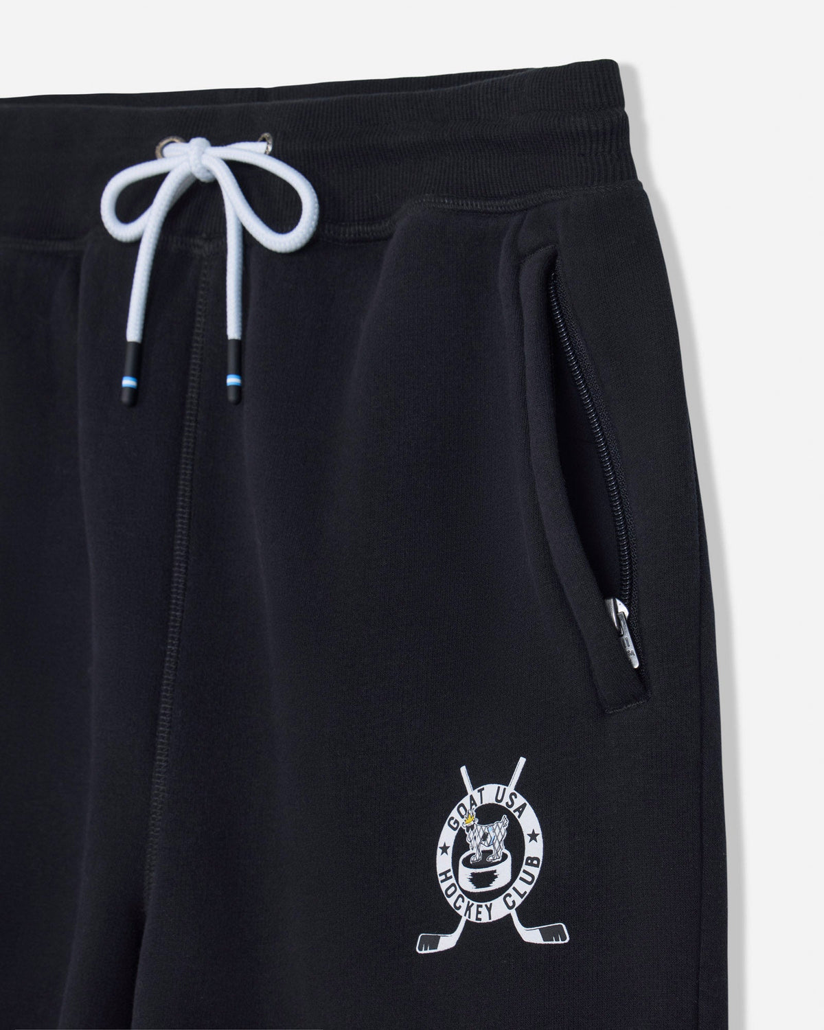 Close-up of black sweatpants with a white drawstring, side zip pocket, and a white hockey-themed crest logo near the lower left leg.