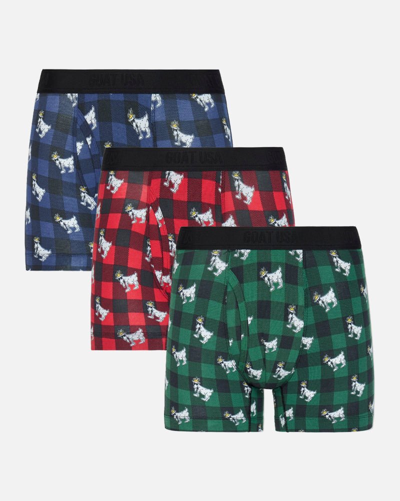 Three pairs of men's boxer briefs in holiday-themed plaid patterns, displayed in a staggered stack on a light gray background. The top pair is navy blue and black with white goat prints, the middle pair is red and black with white goat prints, and the bottom pair is green and black with white goat prints.