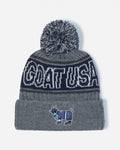 A gray and navy blue knit beanie with a gray pom-pom, featuring 'GOAT USA' in white lettering on a navy band and a small goat mascot patch on the front cuff.