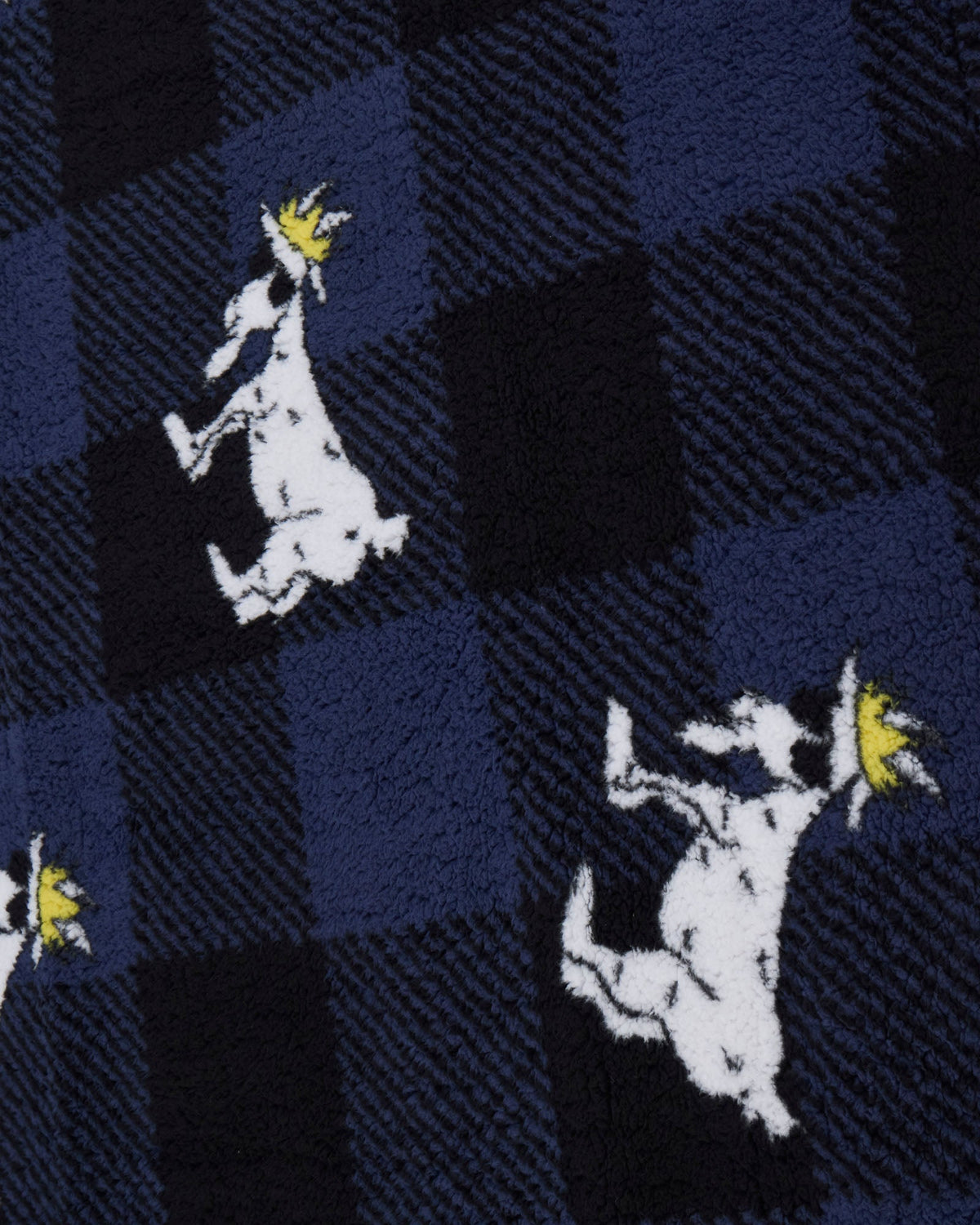 Close-up of a knit fabric with a navy and black plaid pattern, featuring white goat silhouettes holding yellow crowns.