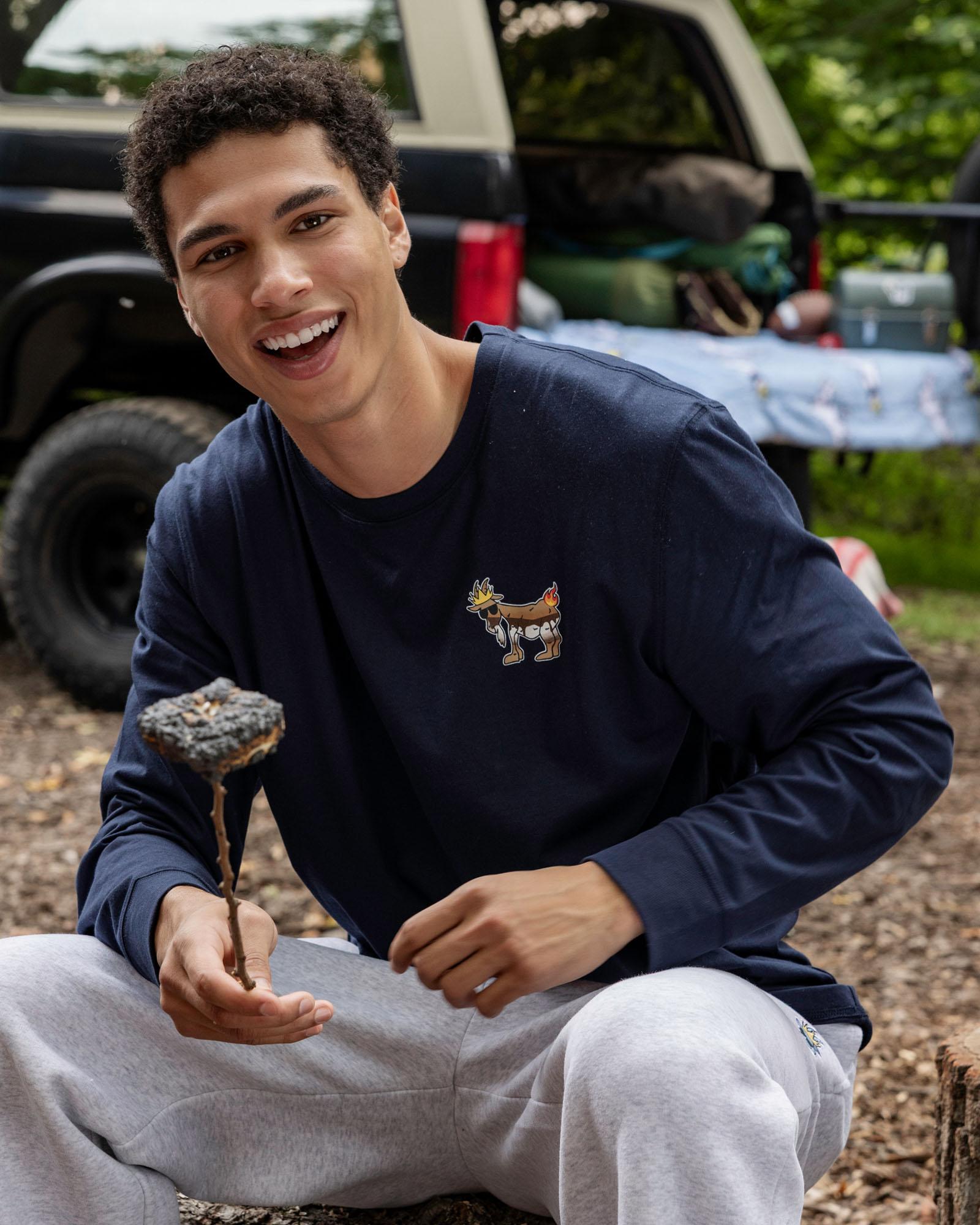 Person wearing a navy blue sweatshirt with a logo, sitting outdoors with a vehicle in the background.