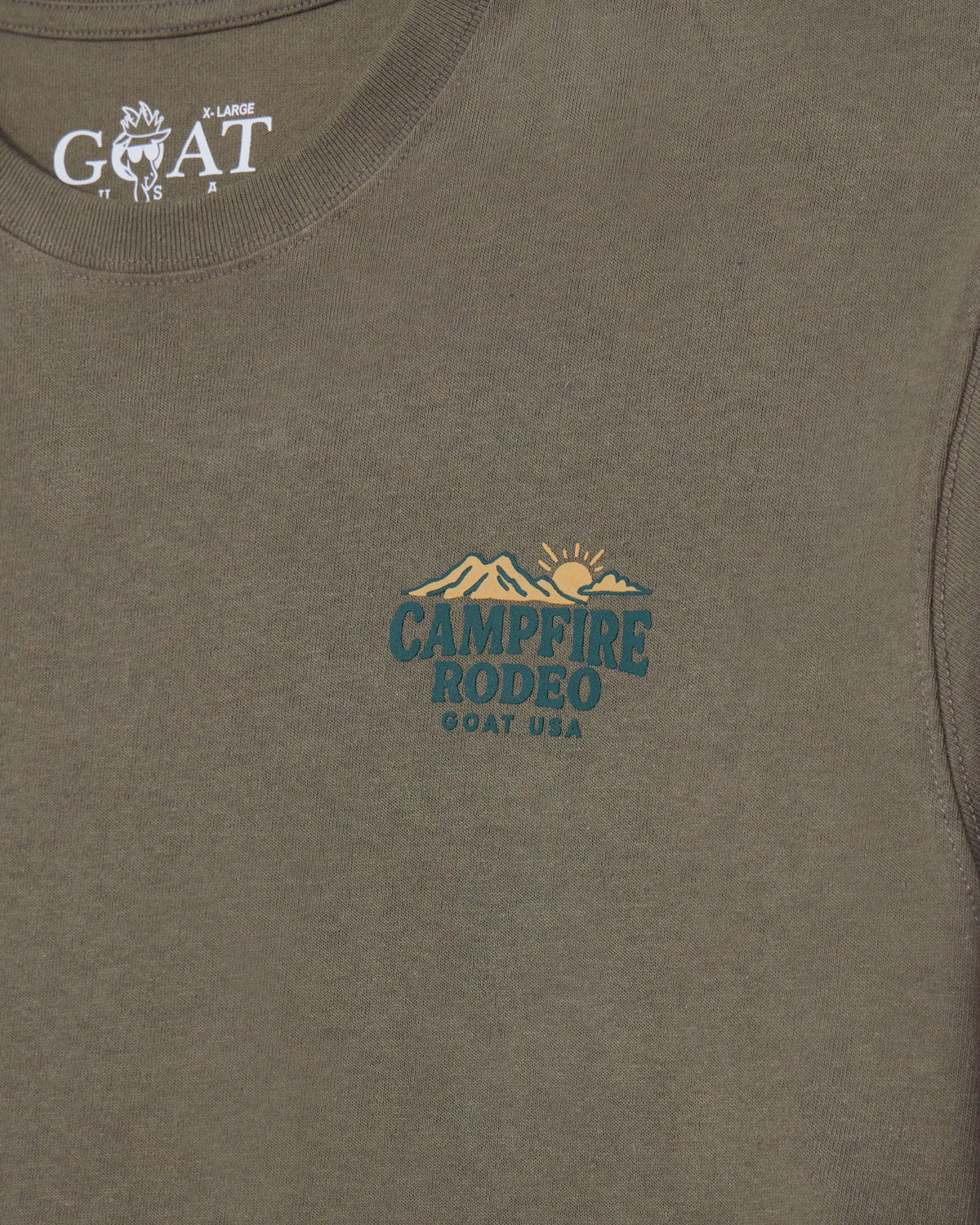 Close-up of a heathered olive-brown t-shirt showing the inner neck label with 'GOAT USA' and a central chest graphic for 'CAMPFIRE RODEO GOAT USA' in teal and tan.