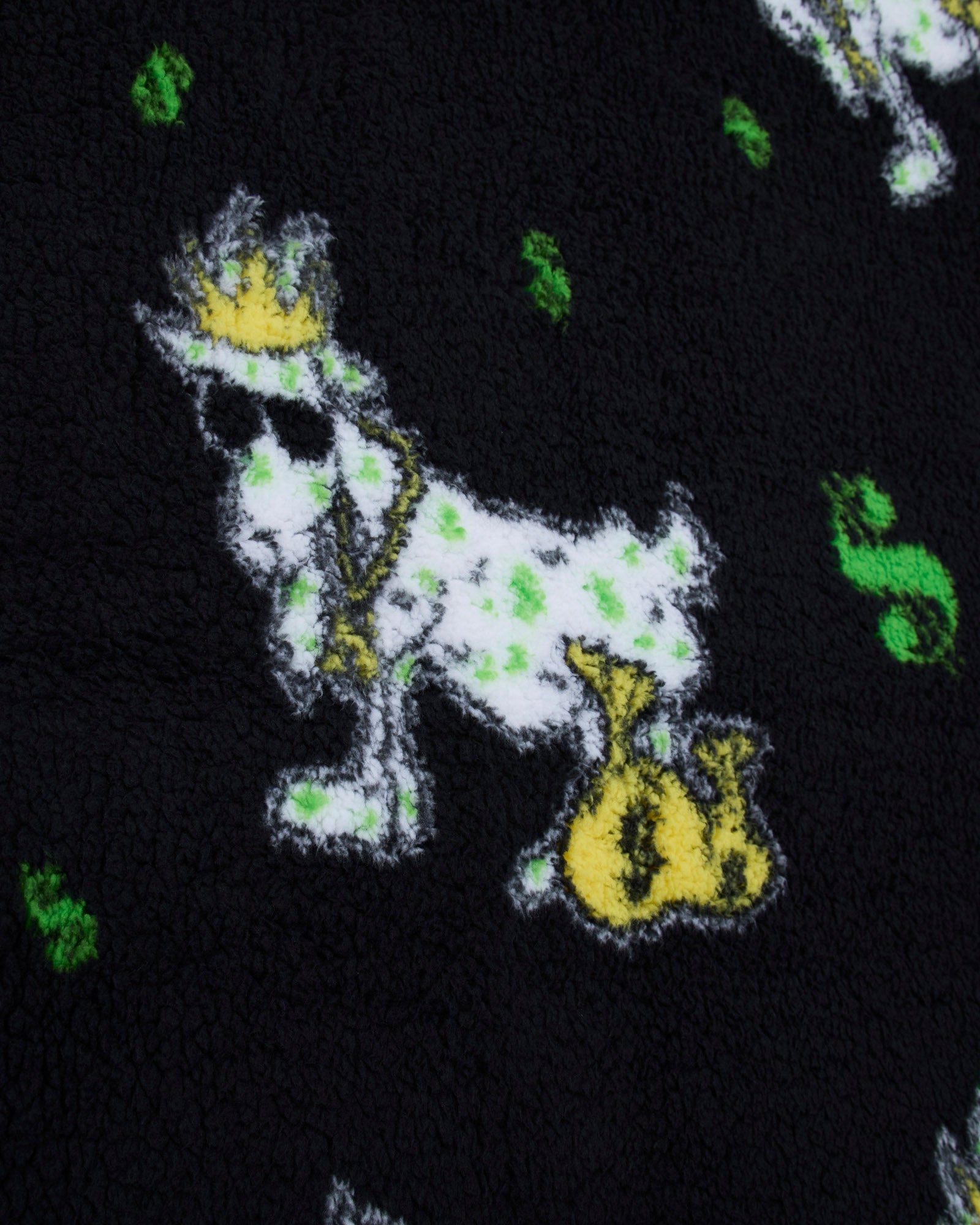 Close-up of a plush black fabric featuring a white goat wearing a gold crown and holding a gold money bag, with small green dollar-sign motifs scattered around.