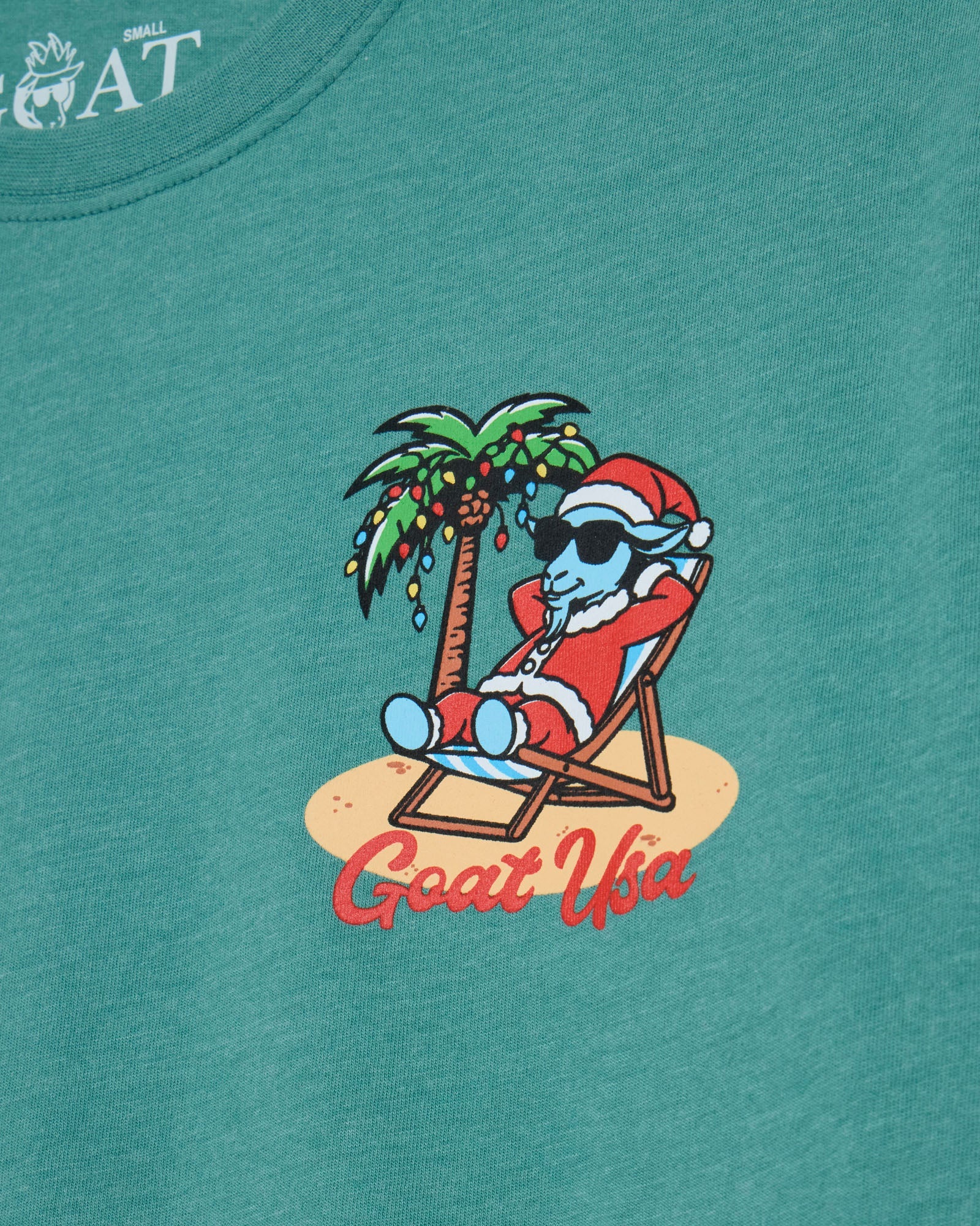 Teal t-shirt with a graphic of a cartoon character in a Santa hat relaxing on a beach chair, palm tree, and 'Goat USA' text.