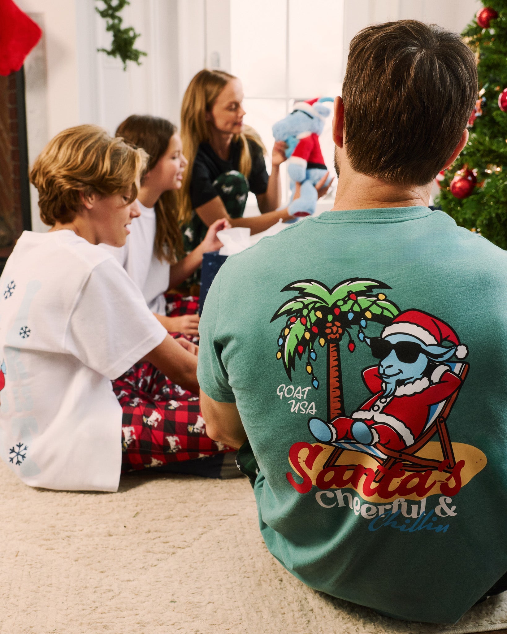 Person wearing a green t-shirt with a graphic design sitting on the floor with children in a festive indoor setting.