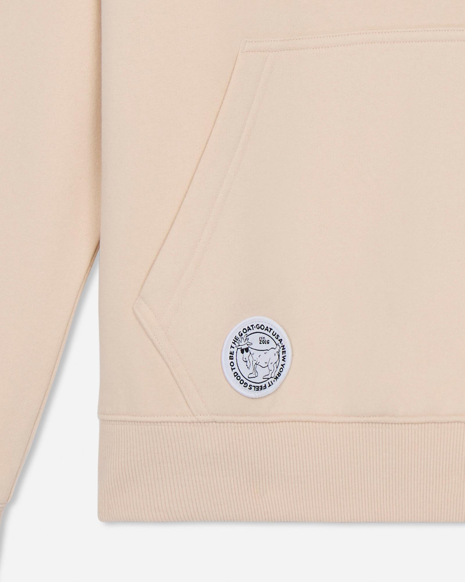 Beige sweatshirt with a logo patch on a light gray background