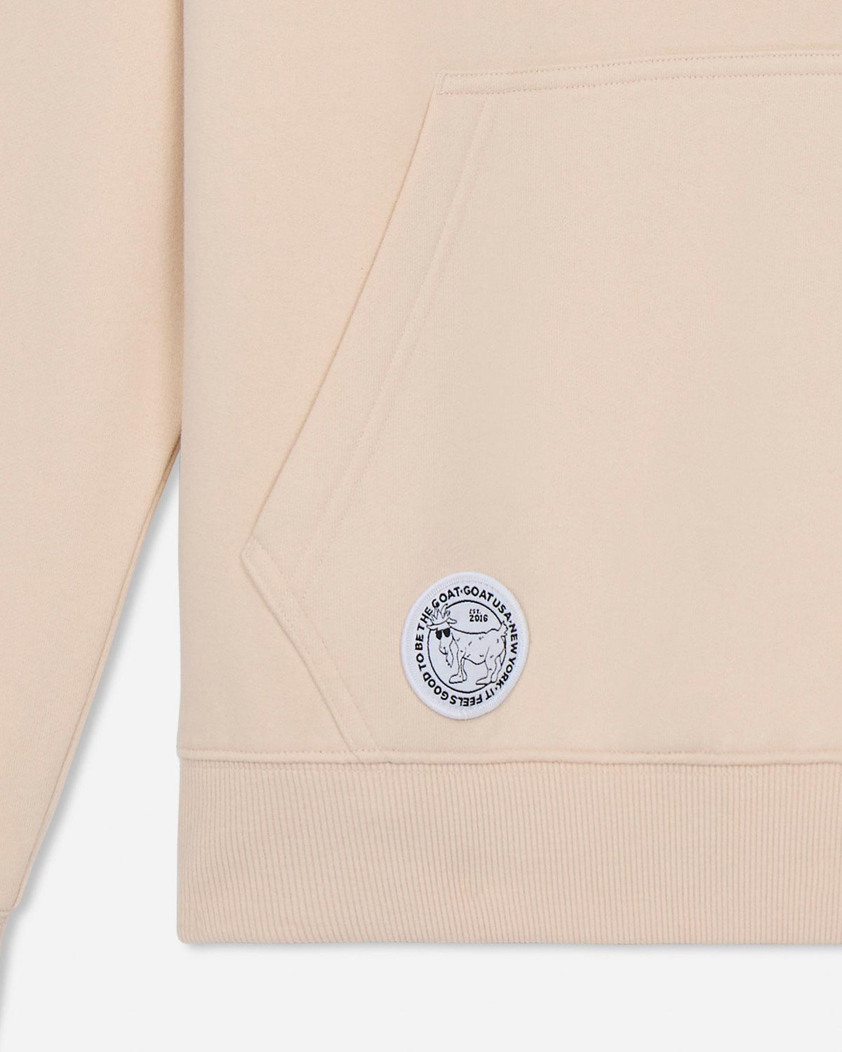 Beige sweatshirt with a logo patch on a light gray background