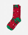 A pair of red crew socks with a green pixelated goat pattern, green heels, and white snowflake details, displayed on a light gray background.