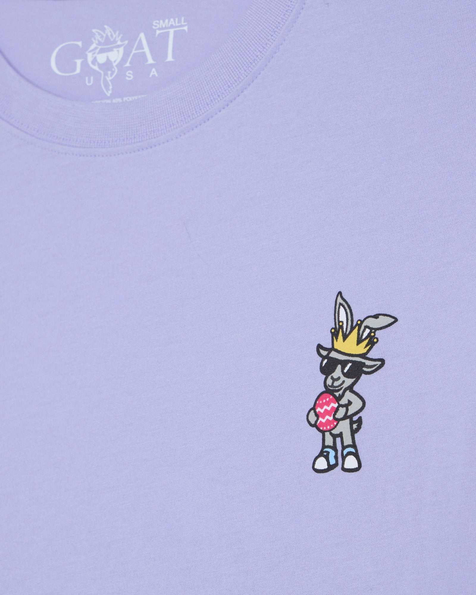 Lavender t-shirt with cartoon goat holding an egg and crown, featuring 'GOAT USA' logo.