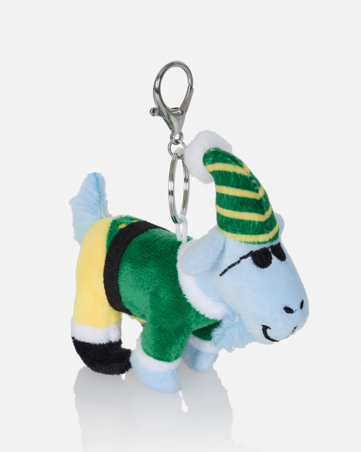A small plush keychain shaped like a cartoon goat wearing a green and yellow striped hat, a green outfit, yellow pants, and black boots, attached to a silver metal key ring on a light gray background.