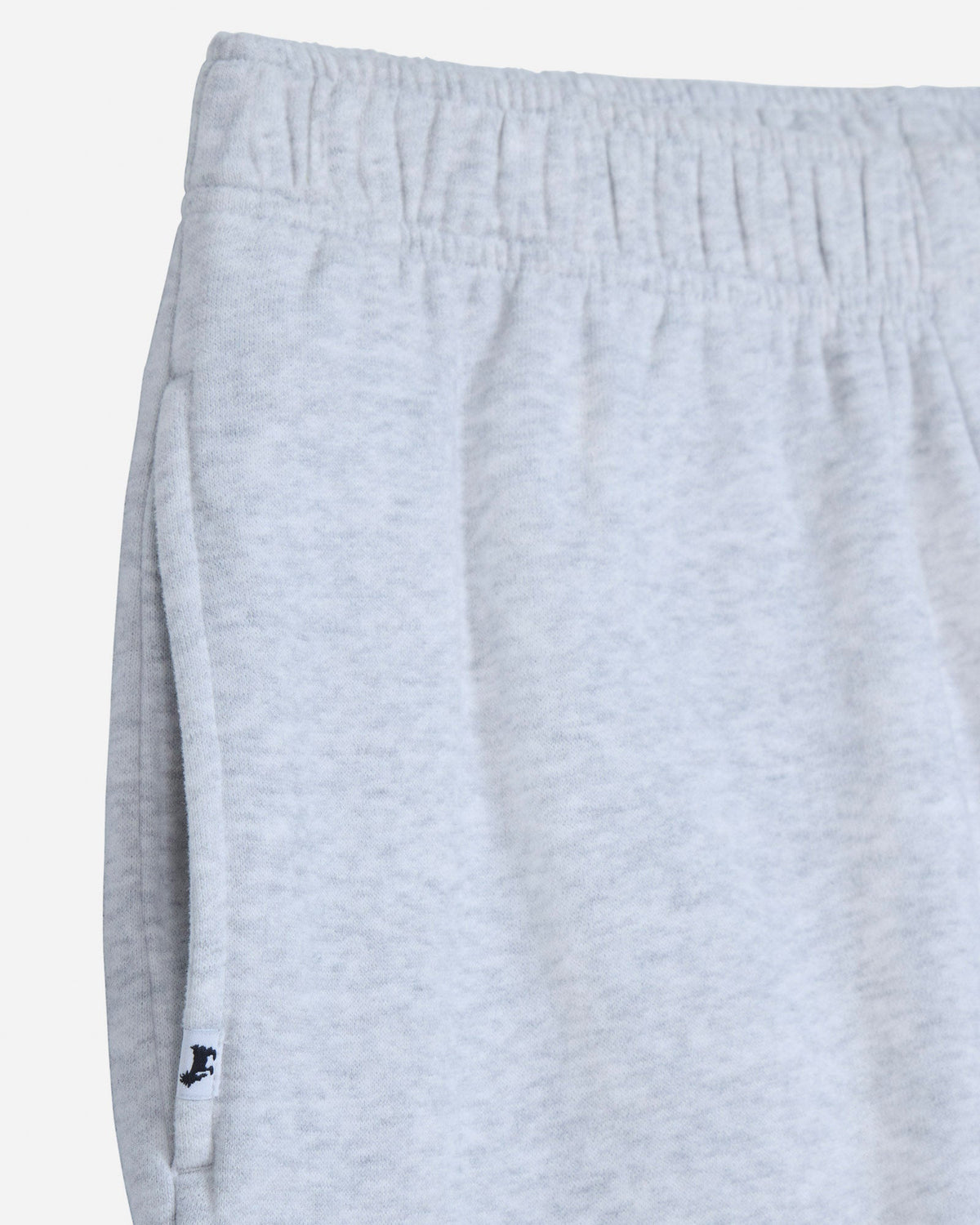 Close-up of light heather gray sweatpants showing the elastic waistband and side seam with a small black embroidered logo near the hem.